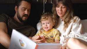 A happy family reading together, featuring parents and their smiling child enjoying a book indoors.